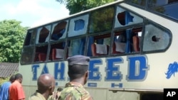 A Kenyan police officer with civilians views a Taheed Bus at the Lamu Police Station in Lamu County, July 19, 2014. 