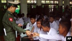 A Burma soldier (L) gives the national identity card to child soldiers who were recruited into the army before reaching the age of 18, during a ceremony where they were handed over to their parents and guardians in Rangoon, September 3, 2012.