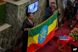 The outgoing prime minister, Haileamariam Dessalegn, who symbolically resigned from his post, hands over the Ethiopian flag to Abiye Ahmed, left, April 2, 2018.