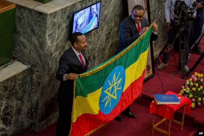 The outgoing prime minister, Haileamariam Dessalegn, who symbolically resigned from his post, hands over the Ethiopian flag to Abiye Ahmed, left, April 2, 2018.