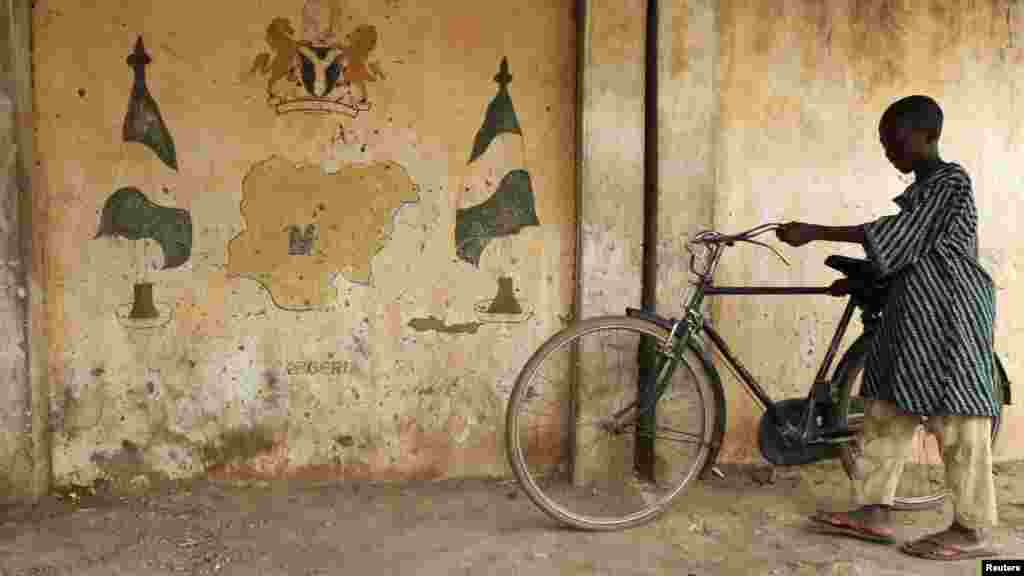 A boy parks a bicycle near a wall, on which the map of Nigeria is painted, in El-kutungu local market in Katsina.