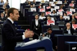 European lawmakers raise placards reading "Stop the War in Syria" in protest against airstrikes launched by the U.S., Britain and France in Syria last week, as French President Emmanuel Macron delivers his speech at the European Parliament in Strasbourg, France, April 17, 2018.