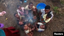 FILE - A Congolese refugee family displaced by fighting between the Congo army and a rebel group, Allied Democratic Forces (ADF), warm themselves around fire at Bukanga transit camp in Bundibugyo, Uganda, July 2013.