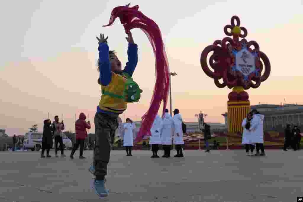 A child plays with a red scarf near a decoration for the Beijing Winter Olympics on Tiananmen Square in Beijing, China.