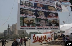 FILE - Egyptian protesters walk under a banner portraying detained journalists. It reads 'The military council protects the former regime.' Another banner calls for 'Media purification,' Tahrir Square, Cairo, Egypt, July 10, 2011