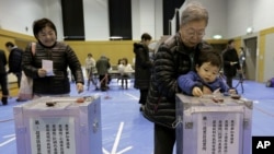 A boy places his grandmother's vote into a ballot box at a polling station in Tokyo, Japan on Dec. 16, 2012.