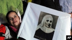 A woman holding a poster of Mother Laura Montoya watches her beatification ceremony on a giant TV screen in her hometown of Jerico, Colombia, May 12, 2013.