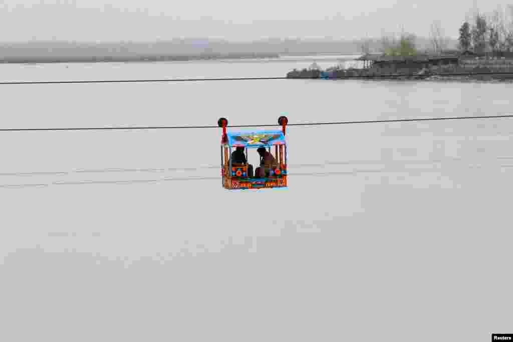 Men sit in a makeshift chairlift to cross a river in Charsadda, near Peshawar, Pakistan.