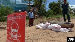 FILE - A Cambodian Mine Action Center (CMAC) member (L) and policeman keep watch behind a Mark 82 bomb in Kandal province on May 21, 2015. 