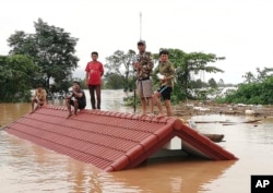 ພວກເຄາະຮ້າຍຈາກໄພພິບັດເຂື່ອນແຕກ ພາກັນໜີຕາຍ ຢູ່ເທິງຫຼັງຄາບ້ານ ໃນແຂວງອັດຕະປື, 24 ກໍລະກົດ 2018.