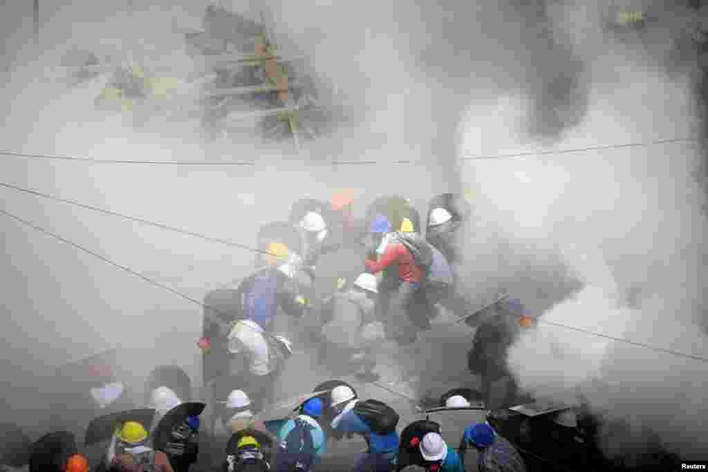 Tear gas and fire extinguisher gas float around protesters as they take shelter behind shields while clashing with riot police during a protest against the military coup in Yangon, Myanmar.