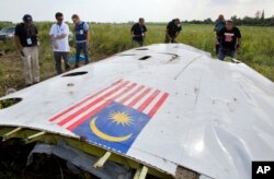 FILE - Malaysian investigators along with members of the OSCE mission in Ukraine, examine a piece of the crashed Malaysia Airlines Flight 17 in the village of Petropavlivka, Donetsk region, eastern Ukraine, July 23, 2014.