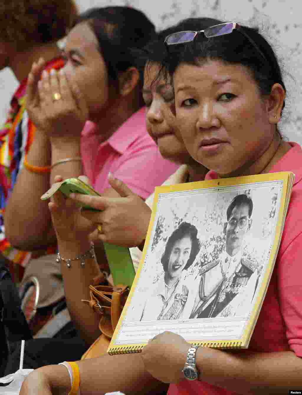 Một phụ nữ cầm ảnh của Vua Bhumibol Adulyadej và Hoàng hậu Sirikit trong khi chờ xe ông rời bệnh viện ở Bangkok, 1/8/13