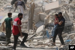 FILE - This photo provided by the Syrian anti-government activist group Aleppo Media Center (AMC), shows a Syrian man carrying a girl away from the rubble of a destroyed building after barrel bombs were dropped on the Bab al-Nairab neighborhood in Aleppo,Syria.