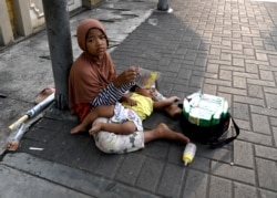 Seorang perempuan dengan bayinya saat dia menjual paket tisu di sepanjang trotoar di Jakarta. (Foto: AFP/ Goh Chai Hin)