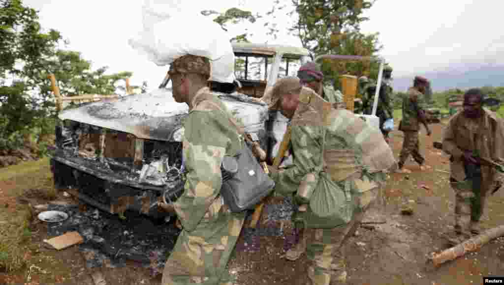 Congolese soldiers carry weapons as they walk near a damaged vehicle after the surrender of M23 rebel fighters in Chanzo village near the eastern town of Goma, Nov. 5, 2013. 