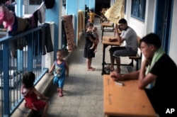 FILE - Palestinians sit outside the classrooms in a U.N. school where families live after their house was destroyed by Israeli strikes, in Gaza City, Sept. 3, 2014.