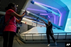 A visitor poses for a souvenir photo next to the replica of missiles weapon used by Chinese military on display at the military museum in Beijing, Thursday, Aug. 1, 2019.