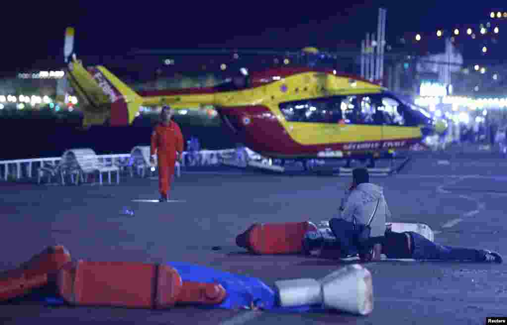 Un blessé couché à même le sol se fait administrer les premiers soins alors qu&rsquo;un hélicoptère de secours a atterri sur lieu après l&#39;attaque de Nice, le 14 juillet 2016 &nbsp;
