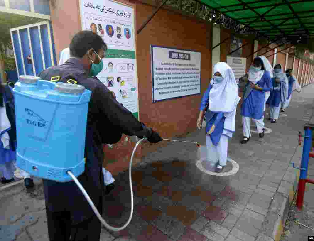 A worker disinfects shoes of a student upon her arrival at a school, in Lahore, Pakistan.