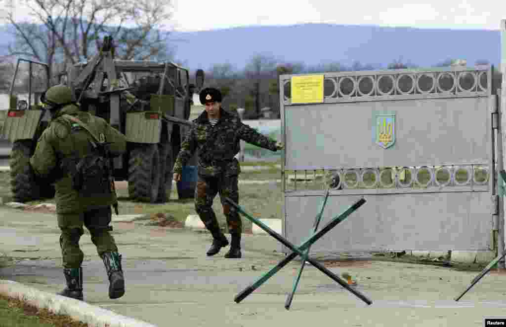 A Ukrainian serviceman closes a gate as an armed man, believed to be a Russian serviceman, stands guard outside an Ukrainian military base in Perevalnoye, near the Crimean city of Simferopol March 13, 2014.