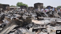 FILE - People stand outside burned houses following an attack by Islamic militants in Gambaru, a city in Nigeria's Borno state, May 11, 2014.