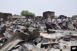 FILE - People stand outside burned houses following an attack by militants in Gambaru, a city in Nigeria's Borno state, May 11, 2014.