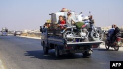 Syrian children ride in the back of a truck loaded with furniture and a motorcycle, driving along the main Damascus-Aleppo highway near the town of Saraqib in Syria's mostly rebel-held northern Idlib province, as families flee north from the countryside, Sept. 11, 2018. 