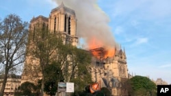 Notre Dame cathedral is burning in Paris, April 15, 2019. Massive plumes of yellow brown smoke is filling the air above Notre Dame Cathedral and ash is falling on tourists and others around the island that marks the center of Paris. 