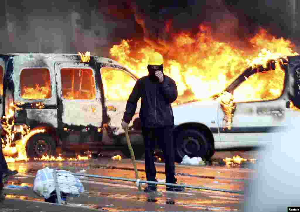 A demonstrator stands in front of burning vehicles during fighting between riot police and demonstrators in central Brussels, Belgium.