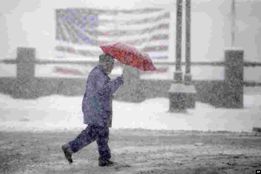 Seorang pejalan kaki melewati bendera AS sementara salju turun di Manchester, New Hampshire. Warga New England terus melakukan kegiatan mereka di tengah-tengah badai musim salju, yang mengakibatkan salju menumpuk hingga hampir 30 cm di beberapa daerah, sementara kawasan tersebut bersiap menghadapi pemilihan pendahuluan calon presiden minggu depan.