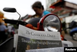 FILE - A woman buys the final issue of The Cambodia Daily newspaper at a store along a street in Phnom Penh, Cambodia, Sept. 4, 2017.