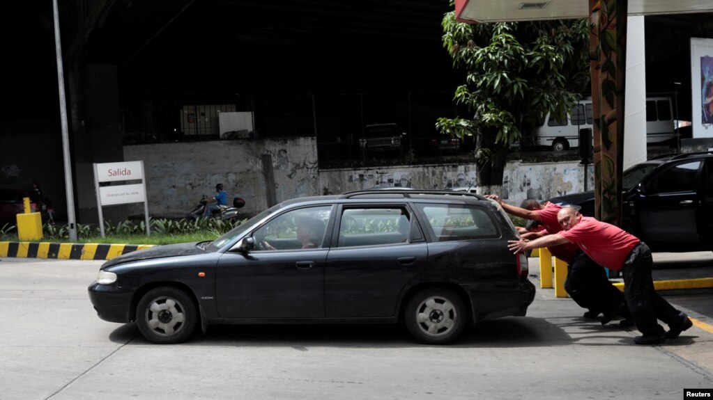 Empleados de una gasolinera empujan un auto en Caracas.