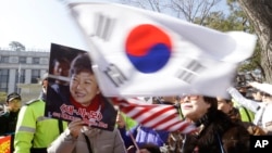 A supporter of impeached South Korean President Park Geun-hye waves flags of the U.S. and South Korea while another holds a portrait of the president during a rally opposing her impeachment in Seoul, South Korea, Feb. 27, 2017. 