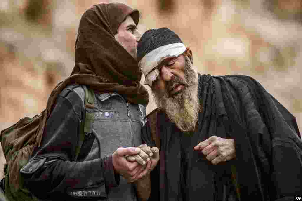 A young man walks with an elderly one injured in his eye with others said to be members of the Islamic State (IS) group as they exit from the village of Baghouz in the eastern Syrian province of Deir Ezzor,