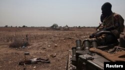 An SPLA military tank drives past the remains of a rebel soldier killed in the frontline at Mathiang near Bor, South Sudan, January 26, 2014.