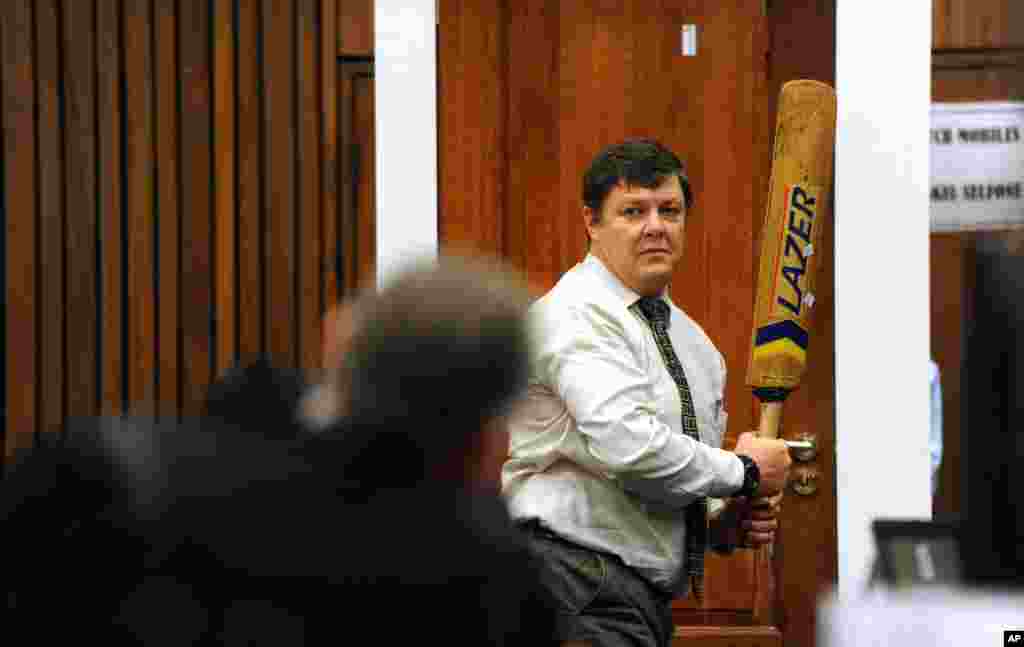 Forensic investigator Johannes Vermeulen, with a cricket bat in hand, demonstrates how Oscar Pistorius could have broken down the bathroom door, Pretoria, March 12, 2014.