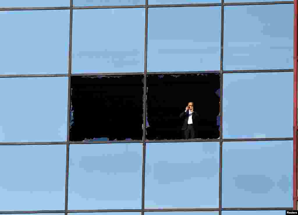 A man looks on from a broken window in front of the scene after a blast in Istanbul, Dec. 11, 2016.