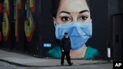 مردی با ماسک از جلوی یک گرافیتی جدید از هنرمند دیوید اسپید می گذرد - شرق لندن، بریتانیا