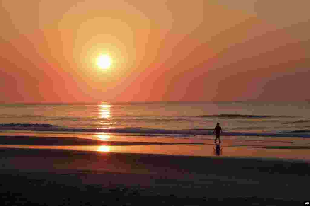 Seorang perempuan berjalan menyusuri pantai saat matahari terbit di pantai Wrightsville, North Carolina, AS.