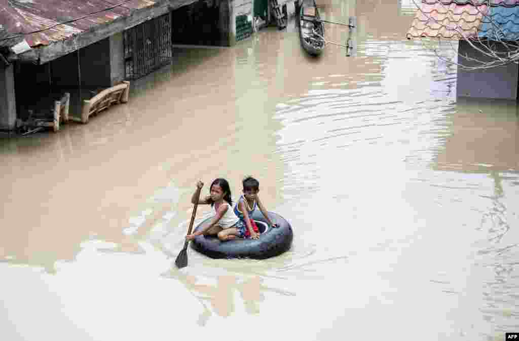 Children use a tire&#39;s interior to cross a flooded street in the aftermath of Super Typhoon Mangkhut at Salonga Compound in Calumpit, Bulacan, Philippines.