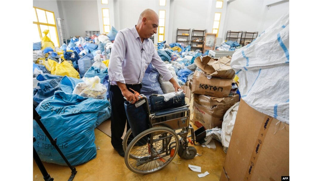 Ramadan Ghazawi, a Palestinian official at the post office in the West Bank city of Jericho, stands next to a folded wheelchair, one of many items of previously undelivered mail in Jericho on Aug. 14, 2018.
