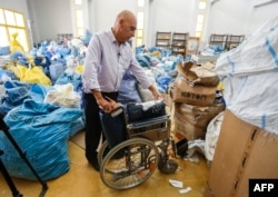 Ramadan Ghazawi, a Palestinian official at the post office in the West Bank city of Jericho, stands next to a folded wheelchair, one of many items of previously undelivered mail in Jericho on Aug. 14, 2018.