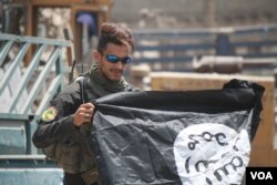 An Iraq soldier poses with an upside-down captured Islamic State flag, July 2, 2017 in Mosul, Iraq. Soldiers say despite their imminent victory in Mosul, the battle with IS is far from over. (H. Murdock/VOA)