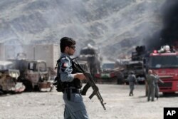 FILE - An Afghan policeman stands guard near burning NATO supply trucks following an attack by militants in the Torkham area near the Pakistan-Afghanistan border in Jalalabad province east of Kabul, Afghanistan, Sept. 2, 2013.