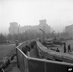 This Nov. 20, 1961 photo shows 12 feet high boards hiding the work as East German troops erect a new concrete wall at the Brandenburg Gate, marking the East-West border in Berlin. In background is the former Reichstag building which is in West Berlin. (AP Photo)