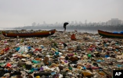 FILE - A fisherman walks on the shores of the Arabian Sea, littered with plastic bags and other garbage, in Mumbai, India, Oct. 2, 2016.