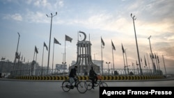 Two men ride their bicycles at Abdul Haq Square with Taliban flags fluttering in the wind, in Kabul, Afghanistan, Dec. 19, 2021. 