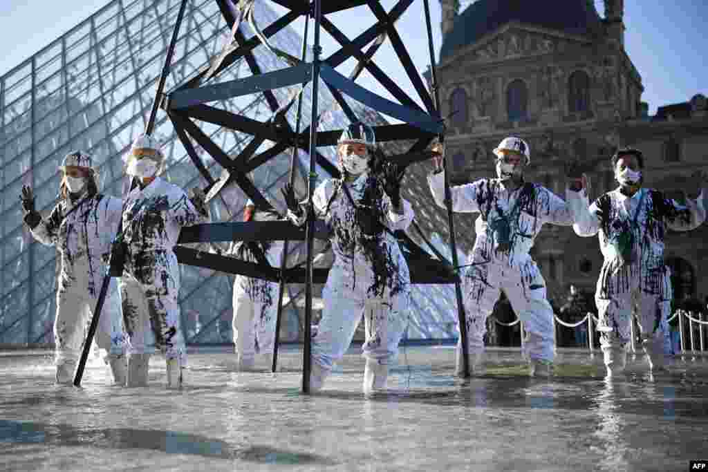 Greenpeace activists wearing the uniform of petroleum workers stand next to a smoking &quot;oil well tower&quot; in front of the Louvre Museum Pyramid in Paris, as they protest against French energy company Total and continued world fossil fuel production and consumption.