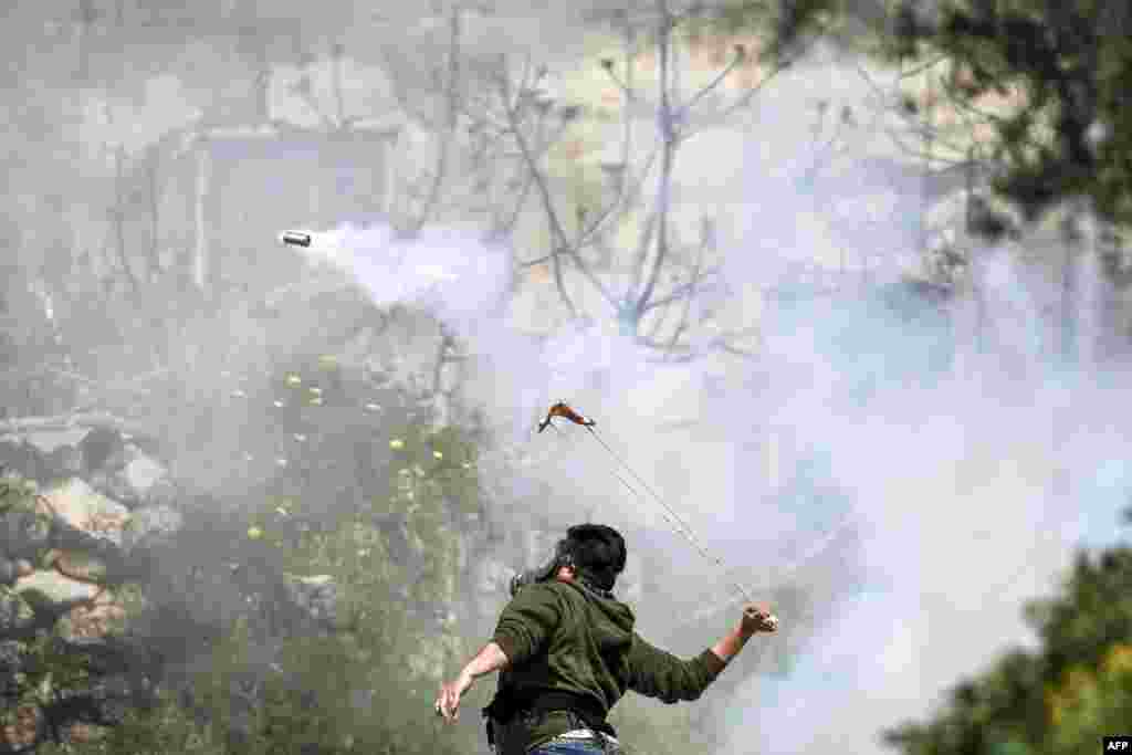 A Palestinian protester wearing a gas mask uses a slingshot to hurl back an Israeli-fired tear gas cannister during clashes in the village of Beit Sira, west of Ramallah, in the Israeli-occupied West Bank, following a demonstration demanding the return of the bodies of those killed by Israeli forces.